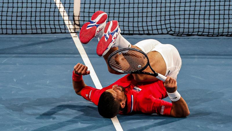 Novak Djokovic de Serbia cae en la cancha mientras juega contra Qinwen Zheng y Zhang Zhizhen de China durante su partido de dobles en el torneo de tenis United Cup.