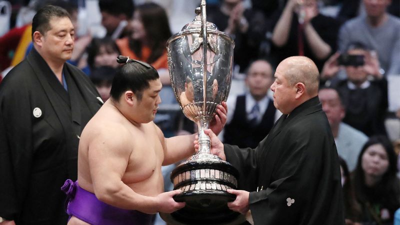 Esta foto tomada el 24 de marzo de 2024 muestra al luchador de sumo de menor ranking Takerufuji (centro izquierda) recibiendo la copa después de ganar el Gran Torneo de Sumo de Primavera de 15 días con un récord superior de 13-2.