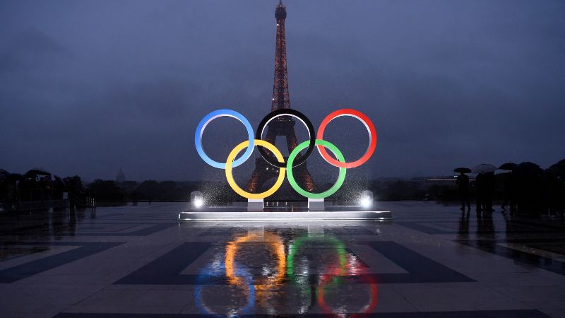 La imagen muestra los anillos olímpicos en la explanada del Trocadero cerca de la Torre Eiffel en París.