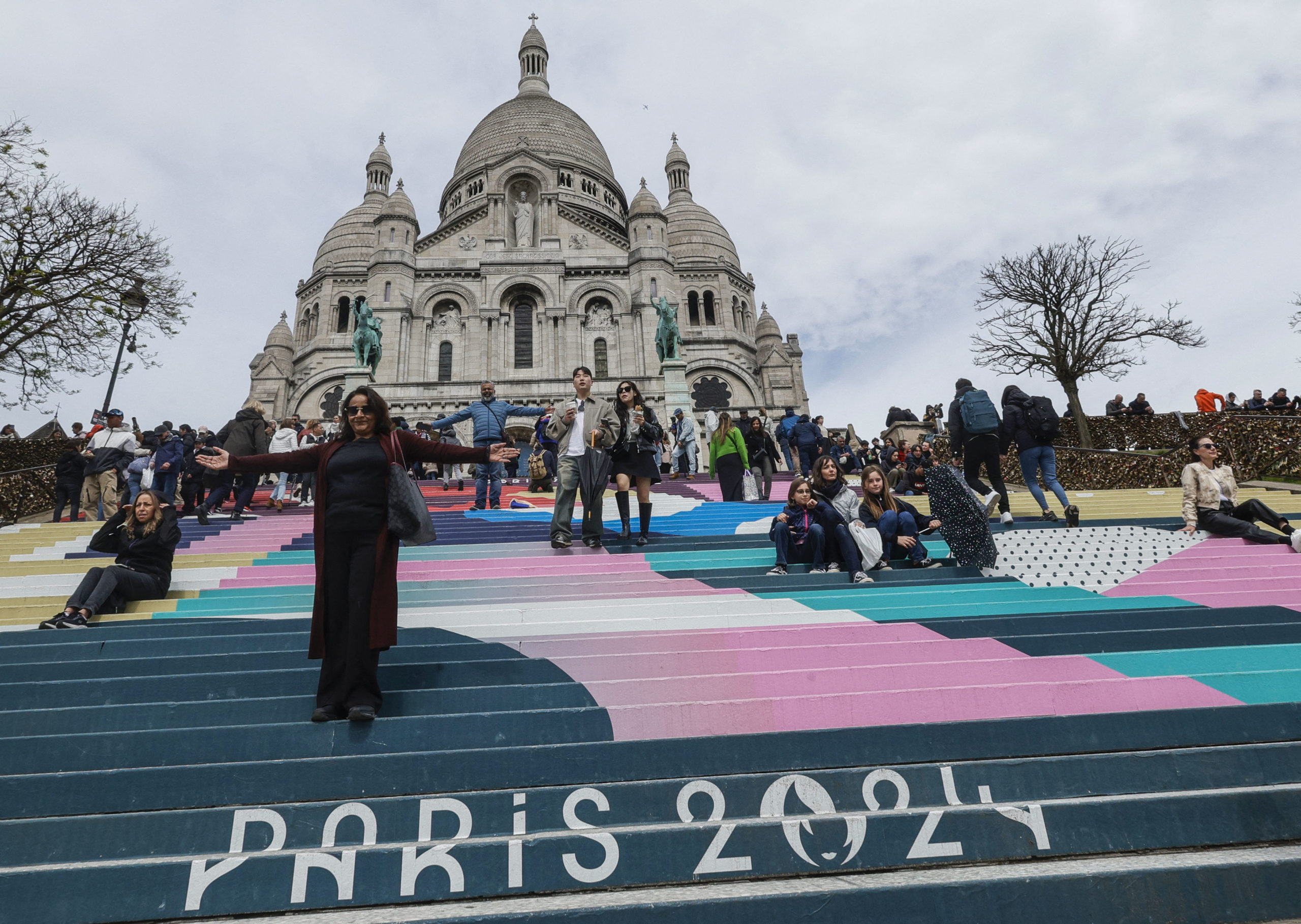 La gente baja las escaleras pintadas con los colores de los próximos Juegos Olímpicos de París 2024 frente a la Basílica del Sacre Coeur.