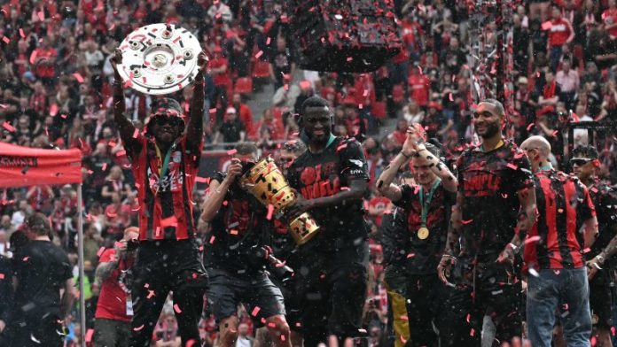 El defensor holandés del Bayer Leverkusen, Jeremie Frimpong, levanta el trofeo de la Bundesliga, mientras el delantero nigeriano Victor Boniface levanta el trofeo de la copa alemana (DFB Pokal).