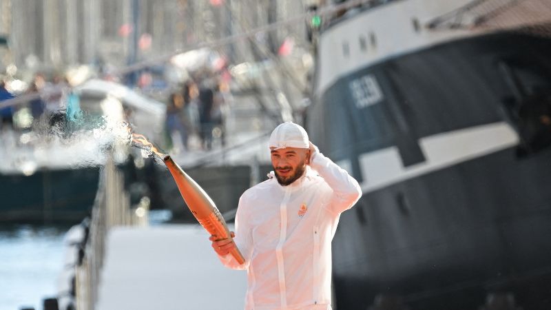 El rapero francés Julien Mari alias Jul sostiene la Antorcha Olímpica, con la barca francesa Belem de tres mástiles del siglo XIX al fondo.