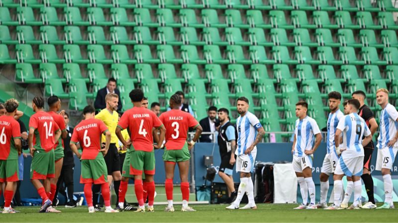 El árbitro sueco Glenn Nyberg observa mientras los jugadores de Argentina y Marruecos se preparan para comenzar a jugar nuevamente en un estadio vacío.