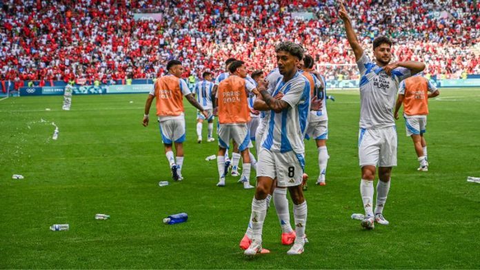 Botellas de agua arrojadas por los fanáticos de Marruecos ensucian el campo mientras el mediocampista argentino, Cristian Medina, celebra después de anotar el segundo gol de su equipo.