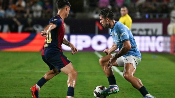 El centrocampista número 10 del Manchester City, Jack Grealish (derecha), controla el balón contra el defensor número 20 del Barcelona, ​​Hector Fort.