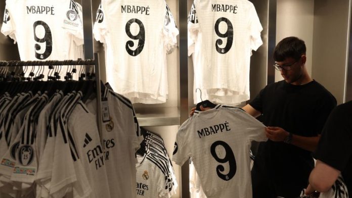 Un hombre sostiene la camiseta recién lanzada del futbolista francés Killyan Mbappé en la tienda oficial del Real Madrid en el estadio Santiago Bernabéu.