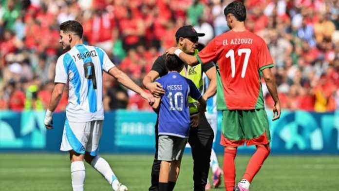 Un joven aficionado que invadió el campo con la esperanza de una foto con el delantero argentino Julián Álvarez es escoltado por un asistente.