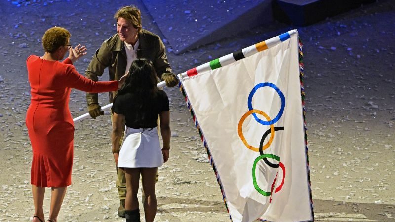 El actor estadounidense Tom Cruise recibe la bandera olímpica de manos de la alcaldesa de Los Ángeles, Karen Bass, y la gimnasta estadounidense Simone Biles durante la ceremonia de clausura de los Juegos Olímpicos de París 2024.