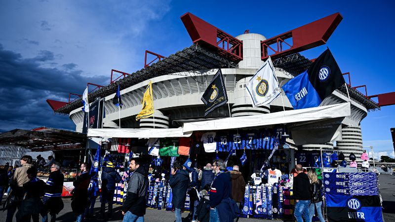 Los hinchas del Inter de Milán caminan junto a bufandas, camisetas de fútbol y artículos de regalo a la venta, fuera del estadio San Siro.