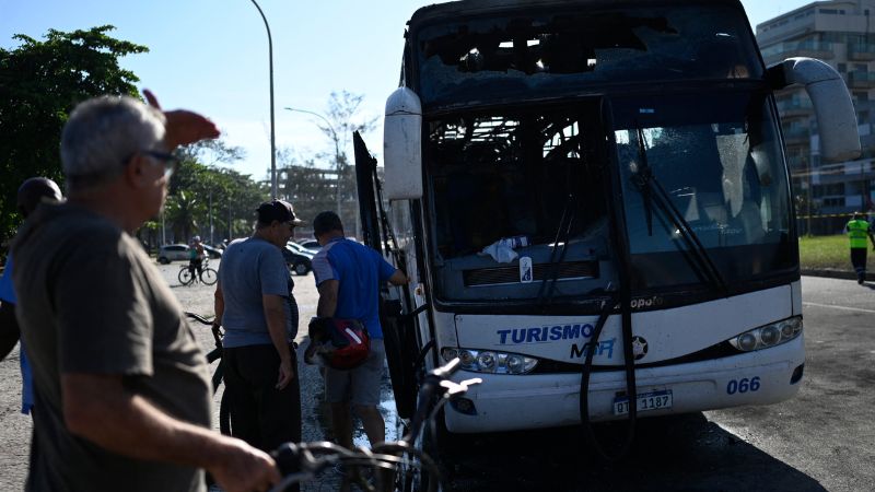 Un grupo de personas observa un autobús quemado durante los enfrentamientos entre hinchas del Peñarol de Uruguay y la policía en la playa Recreio dos Bandeirantes en Río de Janeiro, Brasil.