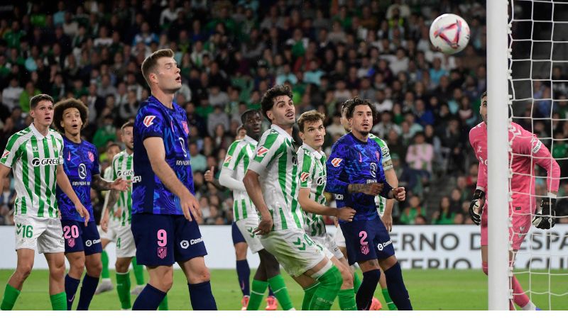 Los jugadores del Betis y del Atlético de Madrid miran fijamente el balón mientras vuela hacia la portería "colchonera".