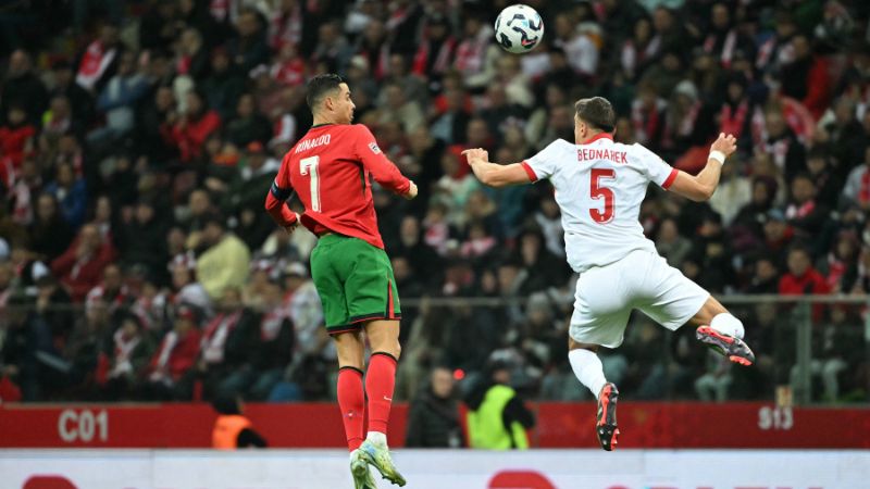 El delantero portugués Cristiano Ronaldo y el defensa polaco Jan Bednarek saltan para cabecear el balón.