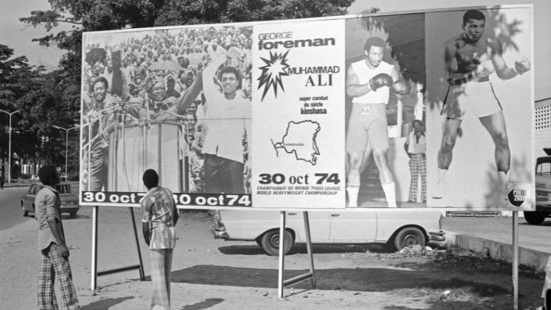 La gente mira un cartel en Kinshasa el 30 de octubre de 1974 que anuncia la pelea entre Muhammad Ali y George Foreman.