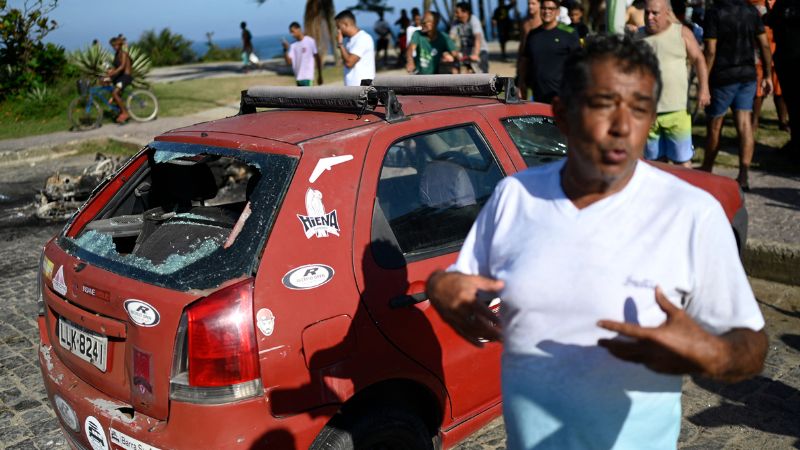 Un hombre habla con miembros de la prensa junto a su automóvil destruido durante los enfrentamientos entre hinchas del Peñarol de Uruguay y la policía en la playa Recreio dos Bandeirantes en Río de Janeiro.