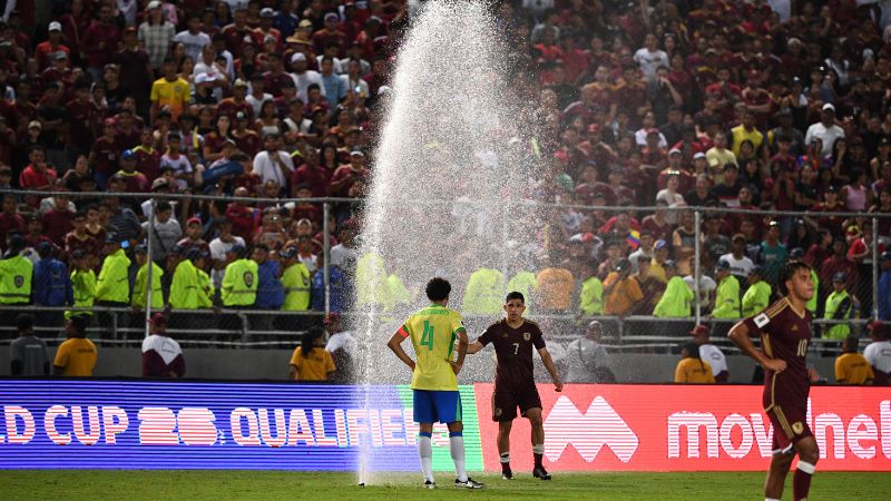 El defensa brasileño Marquinhos y el mediocampista venezolano Jefferson Savarino se encuentran junto a un rociador de agua durante el partido eliminatorio.