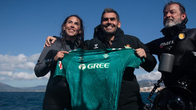 El director de la Fundación Real Betis Balompié, Rafael Muela, junto a unos buceadores sostiene una nueva equipación para el equipo que está hecha de algas y plásticos recogidos del fondo del mar en Tarifa.